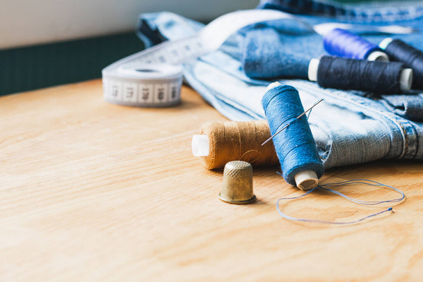 Handicraft, repair and tailoring. Sewing accessories threads close-up denim wooden table. Horizontal frame copy space - Photo, Image