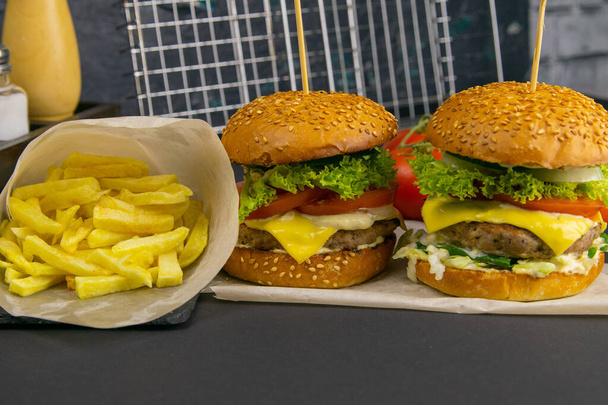 Два гамбургери крупним планом, поруч картопля, помідори, соуси, помідори та перець. Гриль стійка на фоні
. - Фото, зображення