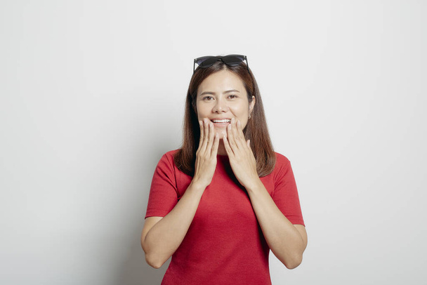 Happy uśmiechnięta piękna azjatycka kobieta gestykulująca rękami i pokazująca dwie ręce dotykające jej twarzy w białym tle ściany.Koncepcja zdrowego i pięknego stylu życia dziewczyny. - Zdjęcie, obraz