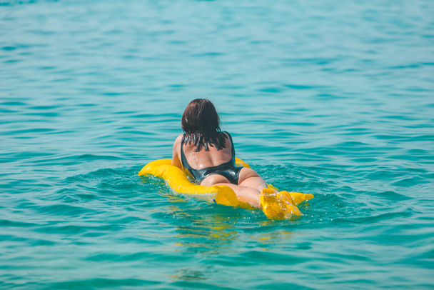femme avec matelas gonflable jaune nageant dans la mer vue de vacances d'été par derrière - Photo, image