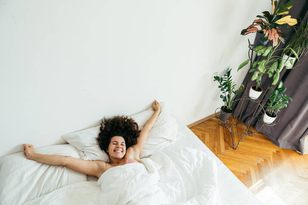 młoda ładna kobieta w łóżku z białymi prześcieradłami jasne światło kopia przestrzeń - Zdjęcie, obraz