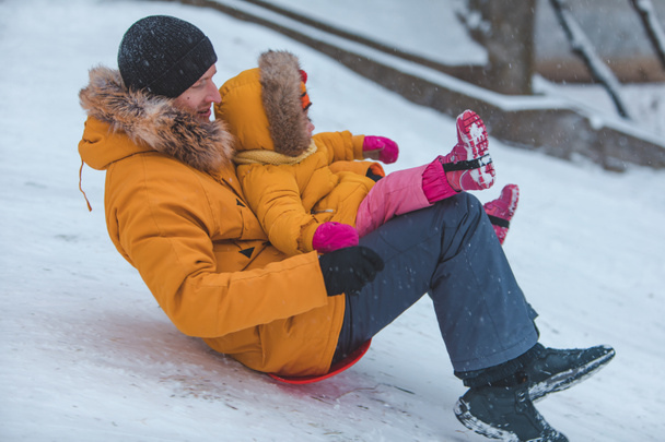 vader met dochter in gele winter jassen glijden sneeuw heuvel familie tijd - Foto, afbeelding