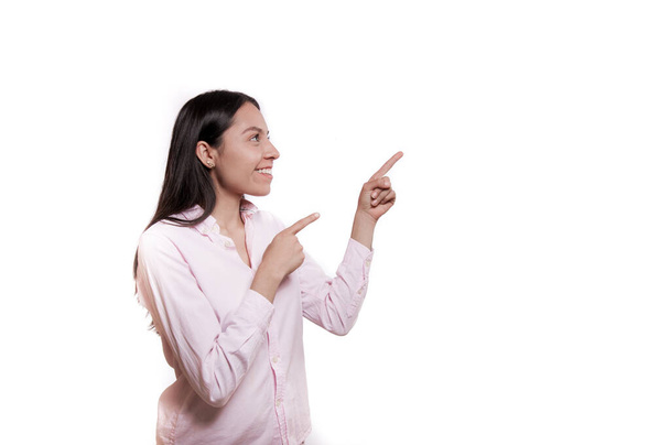 Horizontal studio photograph of an attractive Latin woman with long black hair, dresses in bright clothes, shows a blank space with her index finger, laughs positively suggests following this direction - Photo, Image
