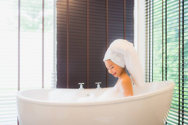 Portret mooie jonge aziatische vrouw gelukkig glimlach ontspannen neem een bad in bad van badkamer interieur - Foto, afbeelding