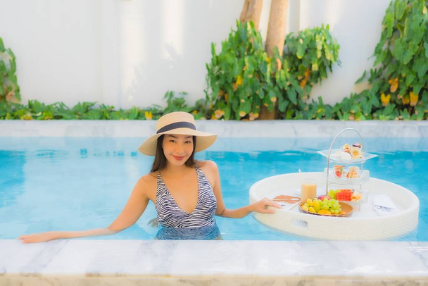 Portrait belle jeune femme asiatique profiter avec thé après-midi ou petit déjeuner flottant sur la piscine dans la station hôtelière - Photo, image