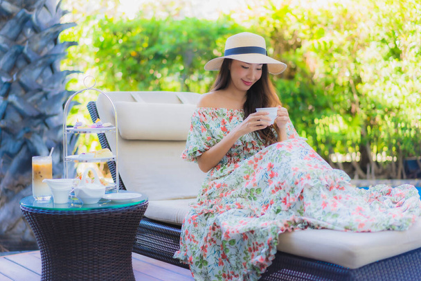Krásná portrét mladá asijská žena s odpolední čaj set s kávou sedět na židli kolem bazénu v hotelovém resortu - Fotografie, Obrázek