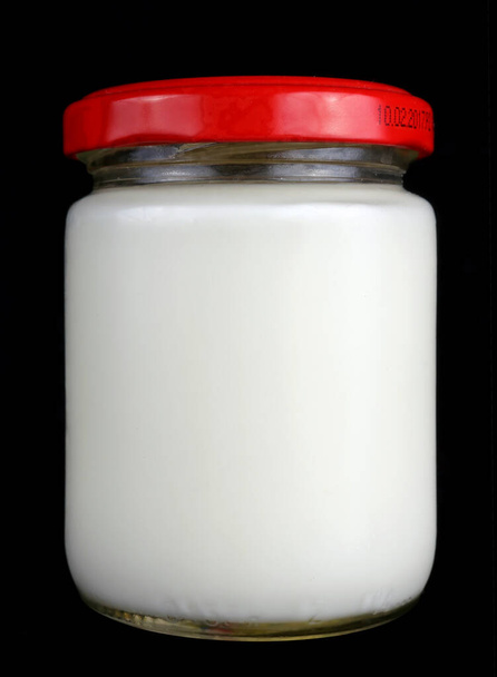 Kleines Einhundert-Gramm-Glas mit weißer Milch und rotem Deckel. Isoliert auf schwarzem Studio-Makro - Foto, Bild