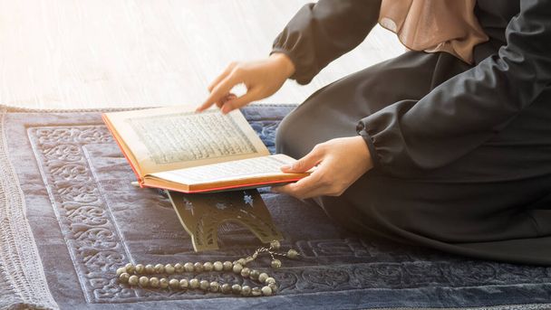 Oříznutý obrázek, Selektivní zaměření na quran na stole, muslimská žena otevření modlitební knihy na modré šedé rohožce spolu s růženec korálky - Fotografie, Obrázek