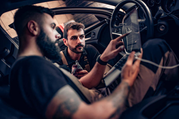 Mecánicos profesionales del coche que trabajan en el servicio de reparación de automóviles. Están utilizando el ordenador portátil mientras se examina el motor del coche
. - Foto, Imagen