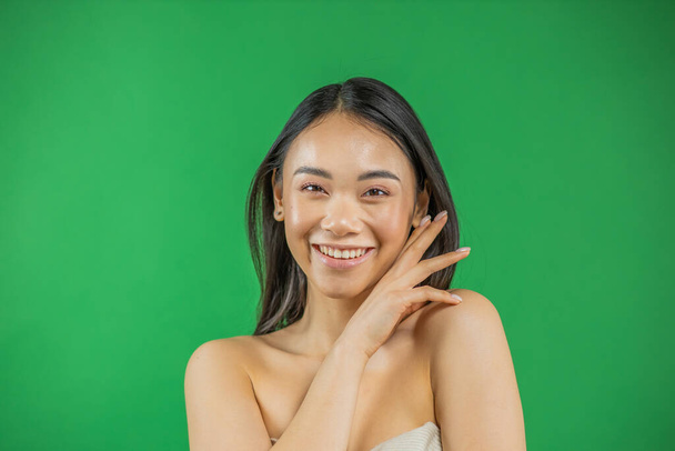 Beautiful young asian woman smiling and looking at camera isolated on green background - Zdjęcie, obraz