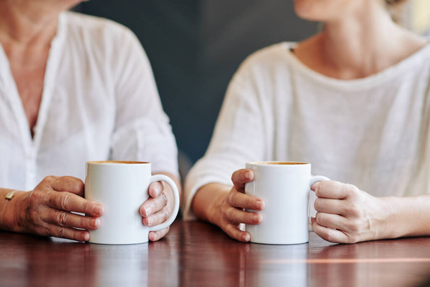 Cropped image of mature woman and her adult daughter drinking coffee and discussing news and gossips at home - Zdjęcie, obraz