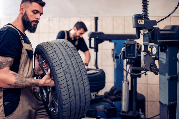 Týmová práce.Mechanik drží pneumatiku v opravárenské garáži. Nahrazení zimních a letních pneumatik. - Fotografie, Obrázek