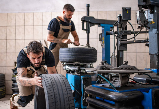 Teamwork. Mechaniker mit einem Reifen in der Werkstatt. Austausch von Winter- und Sommerreifen. - Foto, Bild