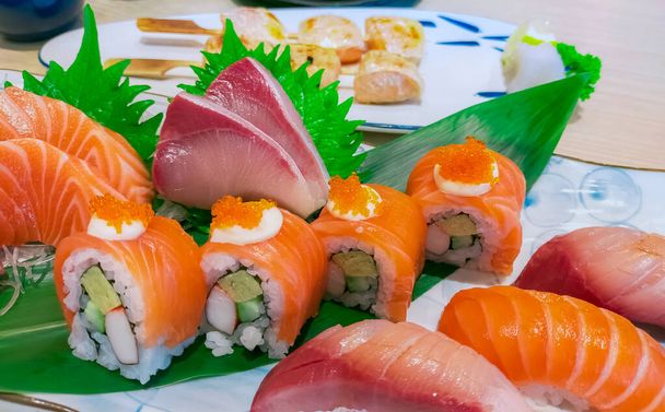 Japanese food combo set on white plate. Salmon sushi, sashimi, and nigiri on restaurant table. Fish meat sliced and Japan vinegared rice rolls with seafood and vegetables. Healthy Japanese food. - Photo, Image
