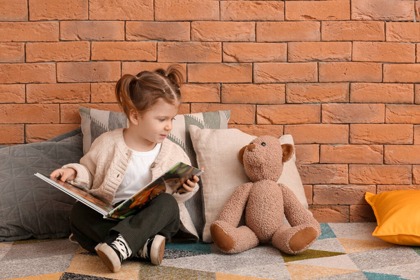 Petite fille mignonne avec ours en peluche livre de lecture près du mur de briques
 - Photo, image