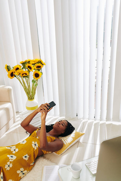 Прекрасна усміхнена молода жінка лежить на підлозі вдома і читає текстові повідомлення формує свого хлопця
 - Фото, зображення