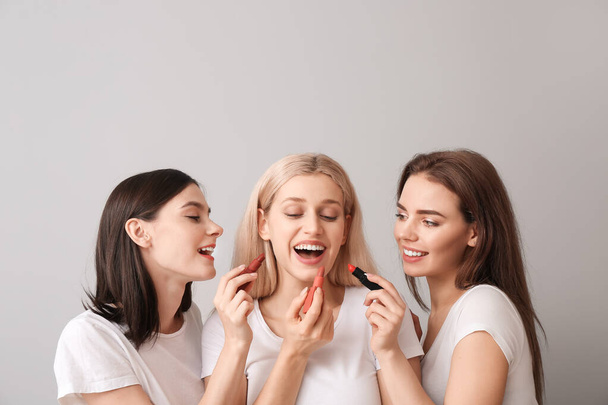 Belles jeunes femmes appliquant le maquillage sur fond clair
 - Photo, image