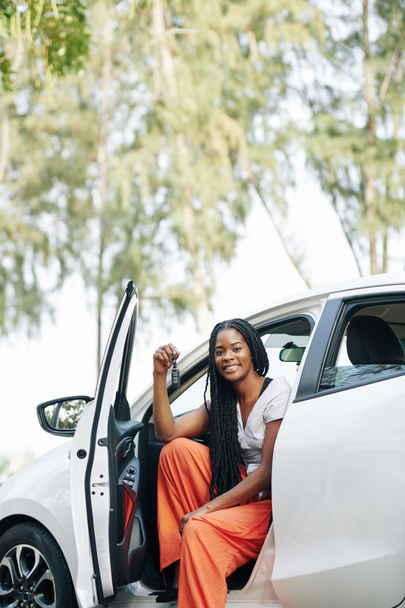 Ευτυχισμένη όμορφη νεαρή μαύρη γυναίκα κάθεται στο νέο της αυτοκίνητο και δείχνει τα κλειδιά - Φωτογραφία, εικόνα