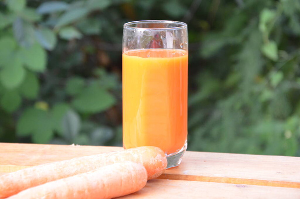 glass of carrot juice and fresh carrots on wooden table on green background - Φωτογραφία, εικόνα