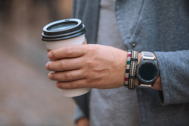 Mann Hand aus nächster Nähe hält Einweg-Kaffeetasse Smart Watch mit Armband am Handgelenk - Foto, Bild