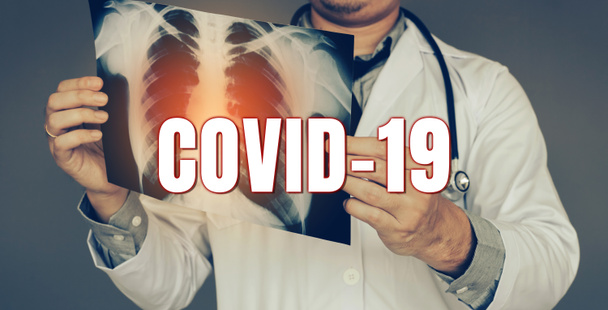 Ο γιατρός μετέφερε μια ακτινογραφία και κοιτάζοντας τη μόλυνση των πνευμόνων νέα ταχέως εξαπλώνεται Coronavirus (Covid- 19) έννοια. - Φωτογραφία, εικόνα