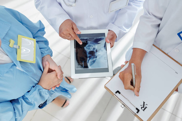 Grupo de médicos discutiendo la radiografía de scull en la computadora tableta y tomando notas en el documento de prescripción
 - Foto, imagen