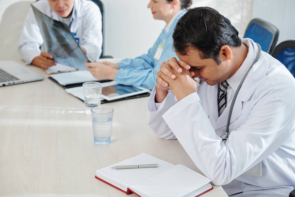 Médico estresado y cansado sentado en la mesa en el salón de médicos
 - Foto, imagen