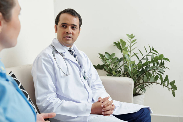 Serious Indian general practitioner talking to female colleague in doctors lounge room - Φωτογραφία, εικόνα