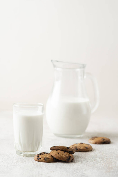 Milk in a jug and chocolate chip cookies on on a white wooden background copy space. - Zdjęcie, obraz