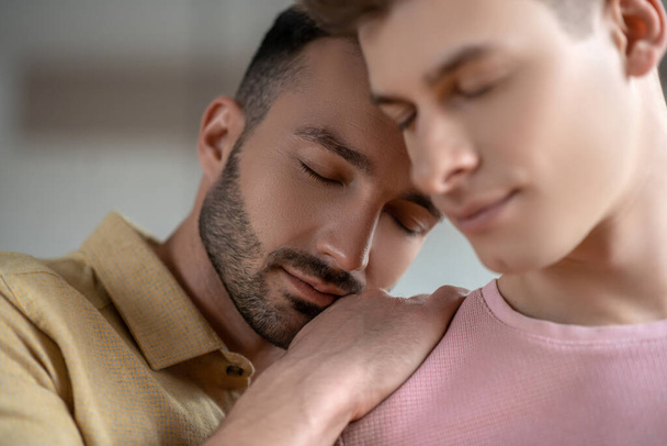 Dark-haired man in orange shirt putting hands on his partners shoulder with eyes closed - Foto, immagini
