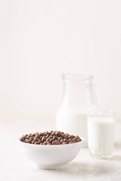 Bowl with chocolate corn balls and milk, on white wooden background. - Valokuva, kuva