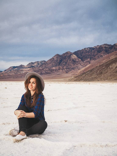 Brunette girl in a plaid shirt with long hair and a gray hat on saline soil Badwater in Death Valley - Foto, Imagen