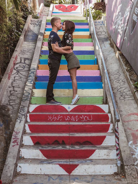Szeretők - a lány a szoknyában és egy fiatalember anomalisa a lépcsőn, lépéseket, amelyek a színek a szivárvány - Fotó, kép