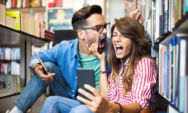 Happy beautiful love student couple taking a selfie in school library. - Photo, Image