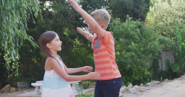 Side view of Caucasian siblings having a good time together in a garden, walking towards each other, embracing, on a sunny day, in slow motion - Filmati, video