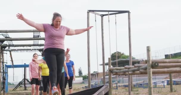 Front view of a happy multi-ethnic group of women enjoying exercising at boot camp together, balancing and walking along a wooden beam in slow motion - Filmagem, Vídeo