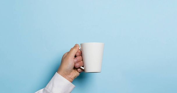 A man holds a cup of coffee or tea drink high in his hand a blue background. Food drink concept. Copy space - Foto, Imagem