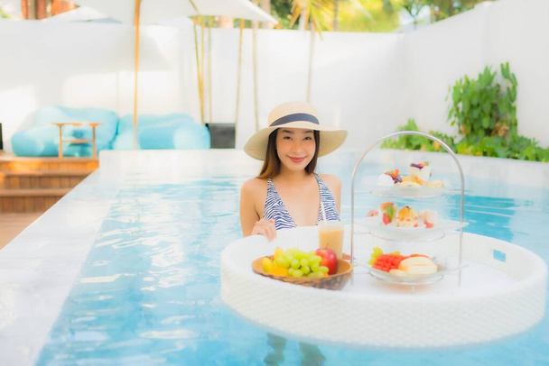 Portret mooie jonge aziatische vrouw genieten met 's middags thee of ontbijt drijvend op zwembad in hotel resort - Foto, afbeelding