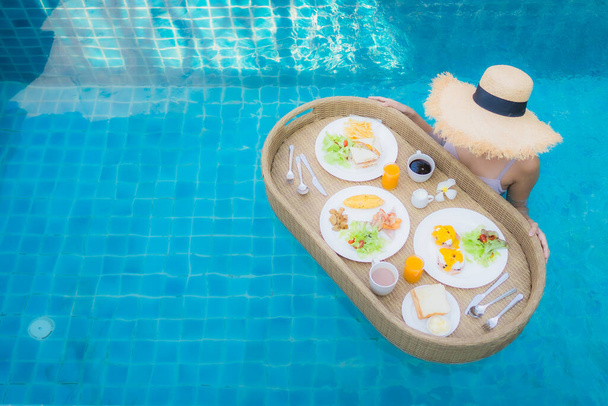 Ritratto giovane donna asiatica sorriso felice godere con vassoio colazione galleggiante in piscina in hotel resort - Foto, immagini