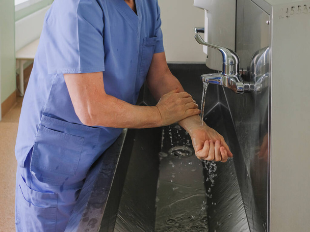 A surgeon washes his hands under a faucet in a stainless steel wash-hand basin. Preparing for a surgical operation. Dysenfection and sterilization. - Фото, зображення