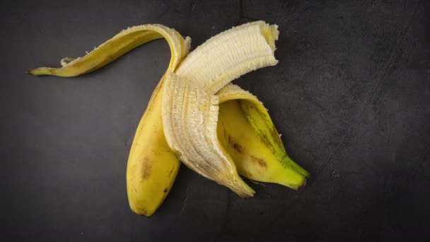 Stop motion video: a banán fokozatosan egyre kisebb. A gyümölcsevés hatása. Az egészséges étel fogalma, a vegetarianizmus. Sötét háttér. 4k - Felvétel, videó