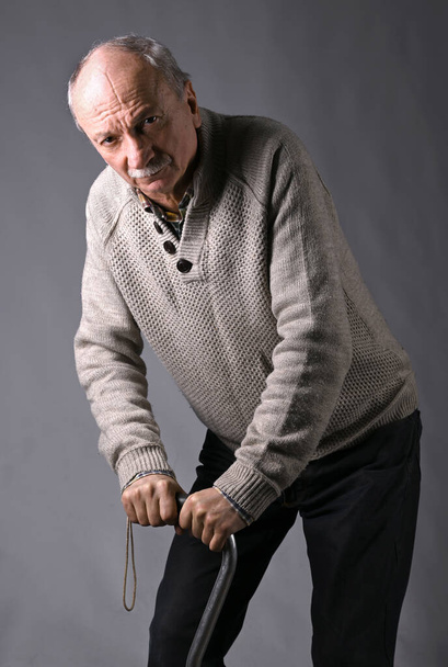Trauriger einsamer älterer Mann mit Stock posiert im Studio vor grauem Hintergrund - Foto, Bild