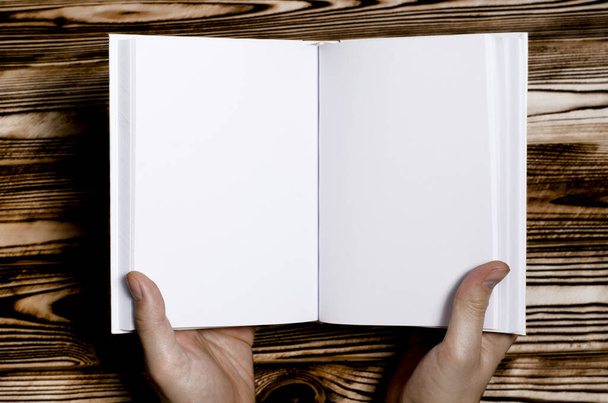 Mãos masculinas segurando livro aberto com tampa em branco no fundo claro. Mockup de livro quadrado em branco aberto
 - Foto, Imagem