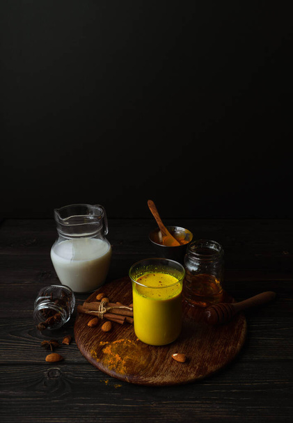 Bardakta vejetaryen zerdeçal latte, badem sütü, koyu ahşap arka planda baharatlar. Kopyalama alanı olan dikey natürmort - Fotoğraf, Görsel