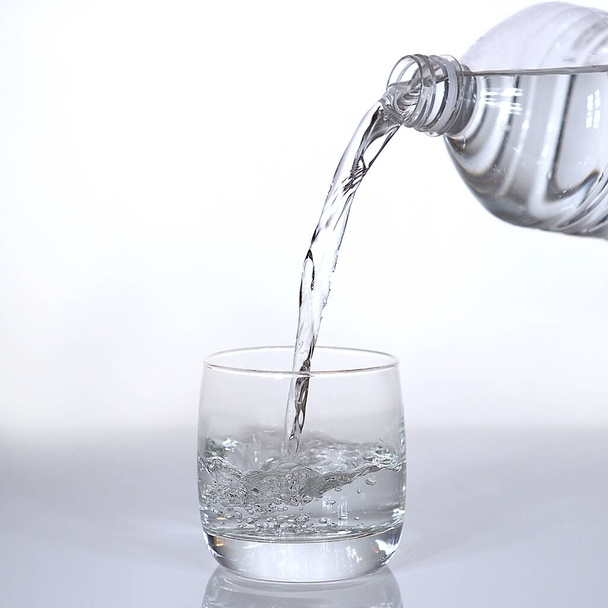 Νερό που χύνεται στο γυαλί σε λευκό φόντο   - Φωτογραφία, εικόνα