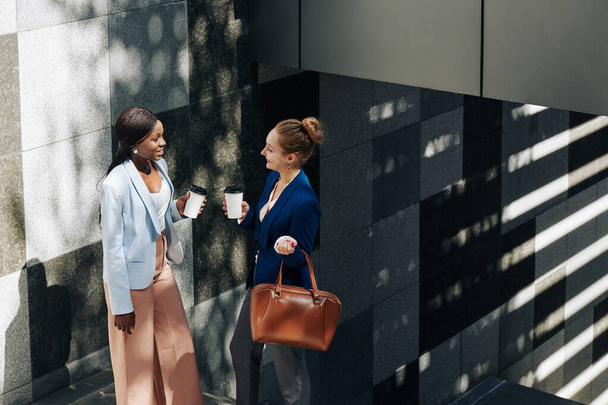Des femmes d'affaires souriantes debout dans les escaliers à l'extérieur avec un café à emporter et des commérages sur le travail - Photo, image
