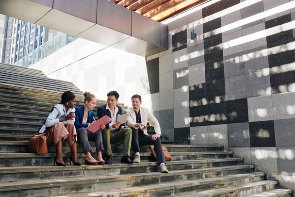 Multi-ethnic business team sitting on steps outdoors and discussing new project - Foto, Imagem