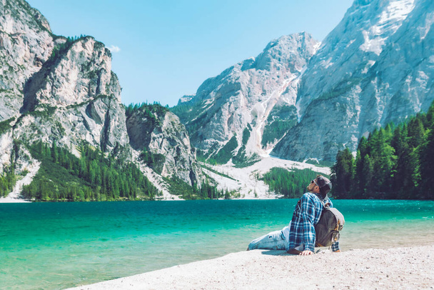 mężczyzna siedzi na plaży nad jeziorem z plecakiem góry w tle włoskie dolomity - Zdjęcie, obraz