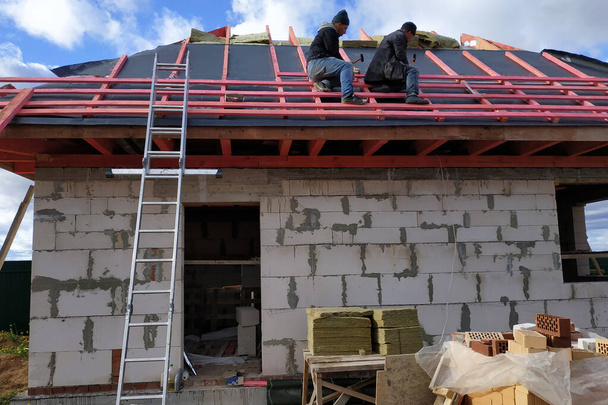 A dolgozók szigetelőanyaggal fedik le a tetőt, szigetelik a hidegtől és a víztől.2020 - Fotó, kép