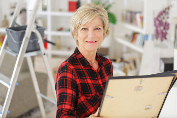 mature woman looking at pisture frame while redecorating - Foto, imagen